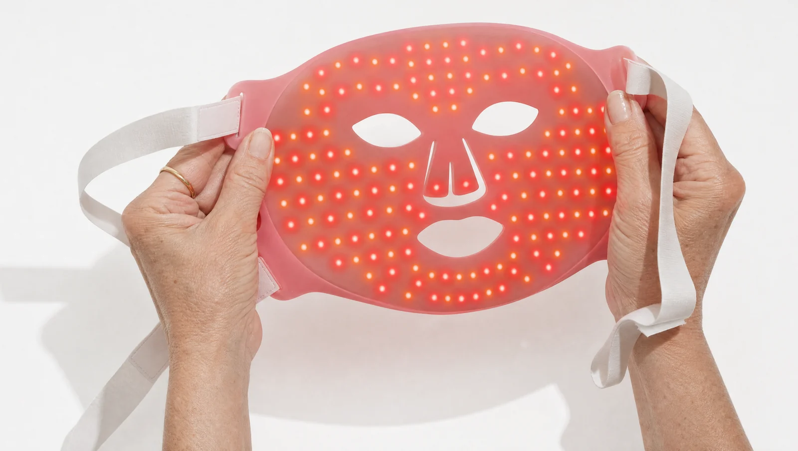 Editorial illustration of two hands holding the Solawave mask open to show the illuminated LEDs