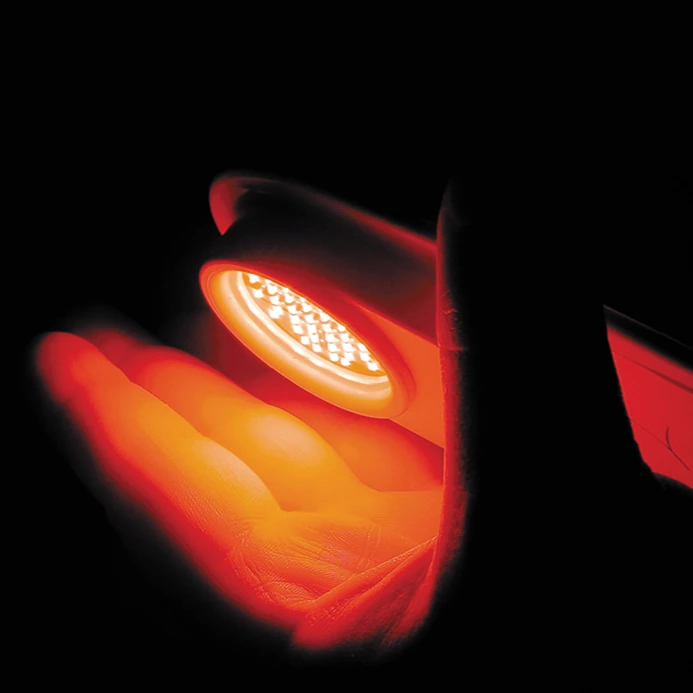 Archival photograph of an early handheld red LED array illuminating a palm for photobiomodulation tissue repair research